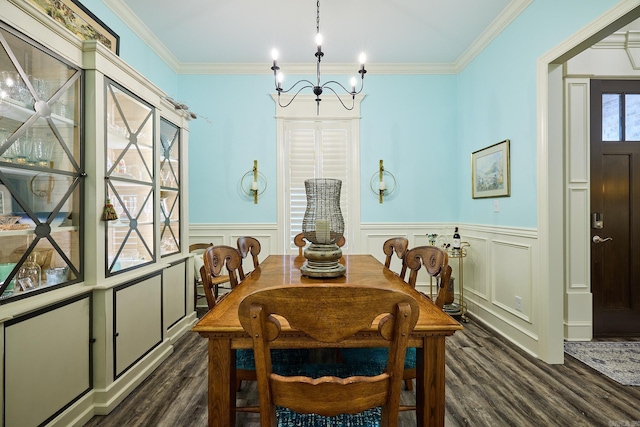 dining room featuring dark wood-style flooring, crown molding, a notable chandelier, a decorative wall, and wainscoting