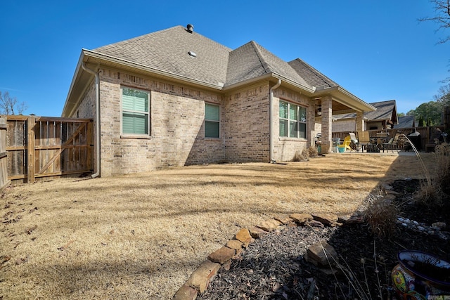 rear view of property with a shingled roof, fence, a patio, and brick siding