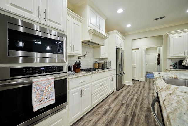 kitchen with visible vents, white cabinets, appliances with stainless steel finishes, ornamental molding, and backsplash