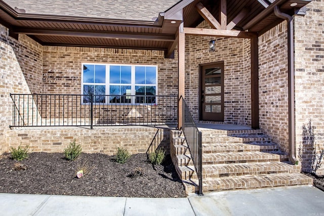 doorway to property featuring a shingled roof, a porch, and brick siding