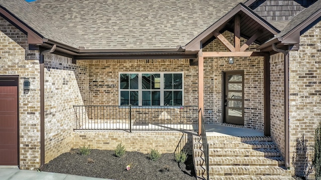 property entrance featuring a garage, covered porch, brick siding, and roof with shingles