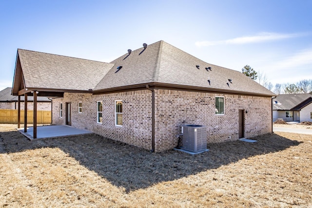 back of property with brick siding, a patio, central AC, and roof with shingles