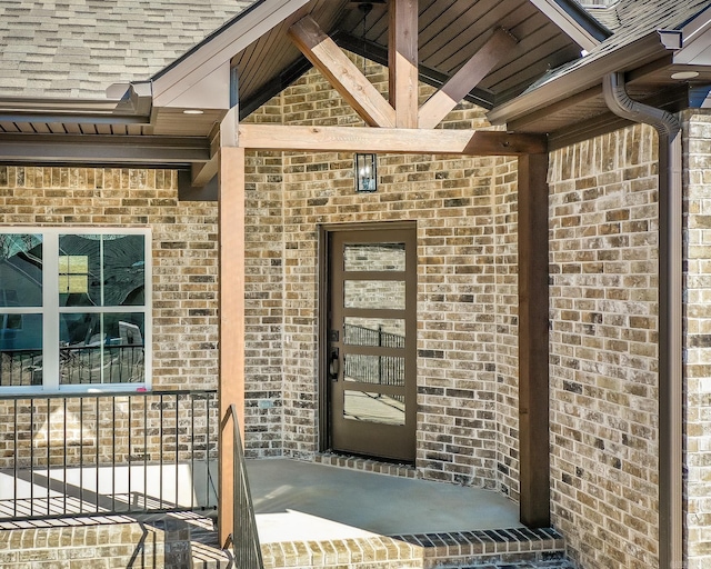 entrance to property with a shingled roof and brick siding