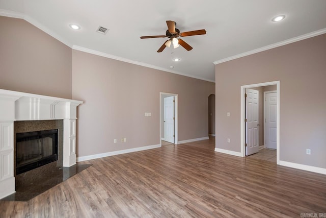 unfurnished living room featuring baseboards, arched walkways, a tiled fireplace, wood finished floors, and crown molding