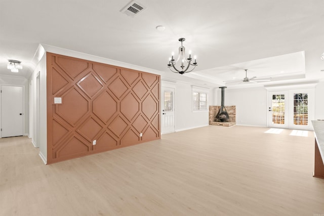 unfurnished living room with visible vents, a raised ceiling, an accent wall, a wood stove, and light wood-type flooring