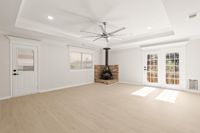 unfurnished living room with a wood stove, light wood finished floors, a raised ceiling, and visible vents