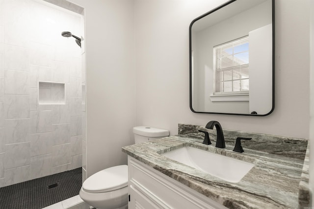 bathroom featuring toilet, a tile shower, and vanity