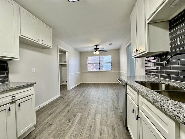 kitchen featuring a sink, a ceiling fan, white cabinetry, light wood-type flooring, and tasteful backsplash