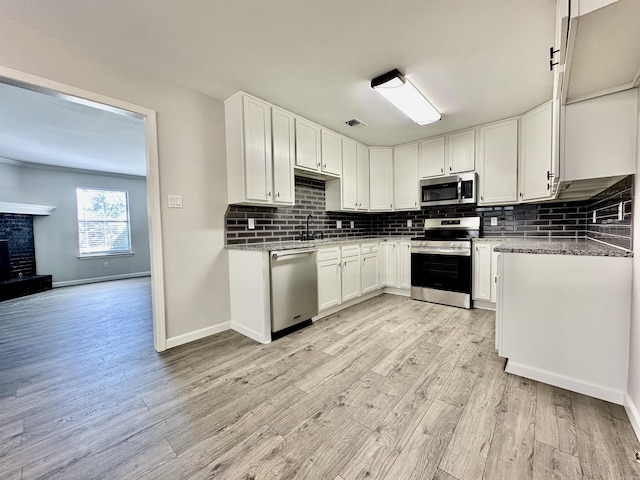 kitchen with stainless steel appliances, white cabinets, light wood-type flooring, a brick fireplace, and tasteful backsplash