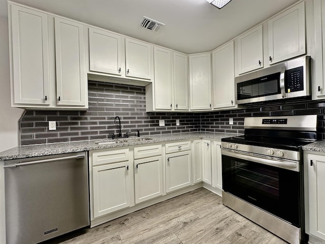 kitchen with visible vents, light wood-style flooring, appliances with stainless steel finishes, a sink, and backsplash