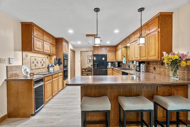 kitchen featuring tasteful backsplash, light wood-style flooring, a kitchen breakfast bar, a peninsula, and black appliances