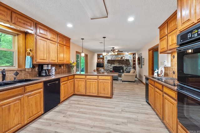 kitchen featuring a fireplace, open floor plan, a sink, a peninsula, and black appliances