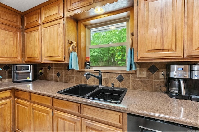 kitchen featuring dishwasher, tasteful backsplash, brown cabinetry, and a sink