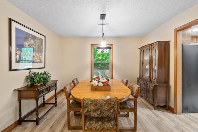 dining area featuring a textured ceiling, baseboards, and light wood-style floors