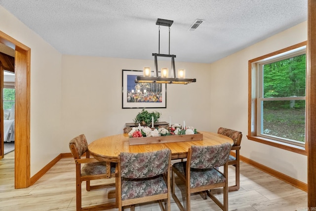 dining room with a chandelier, light wood-type flooring, visible vents, and baseboards