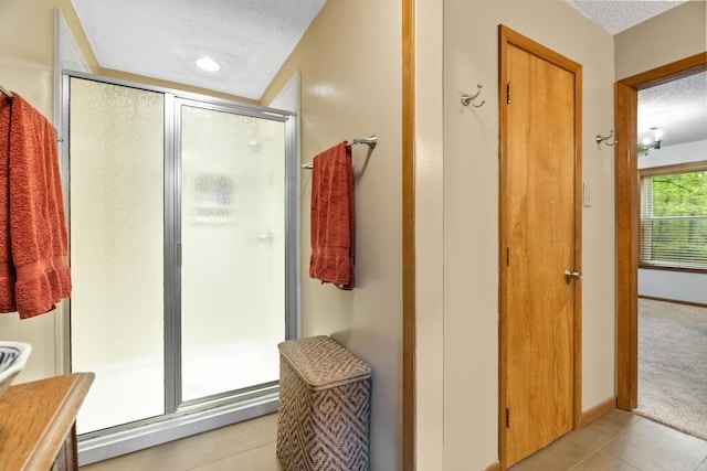 bathroom with a shower stall, baseboards, a textured ceiling, and tile patterned floors