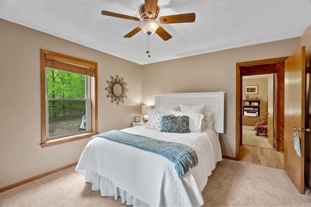 bedroom featuring light colored carpet, ceiling fan, a textured ceiling, and baseboards