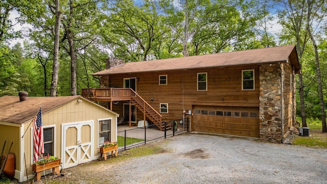 view of front of home featuring driveway, a chimney, an outbuilding, an attached garage, and fence