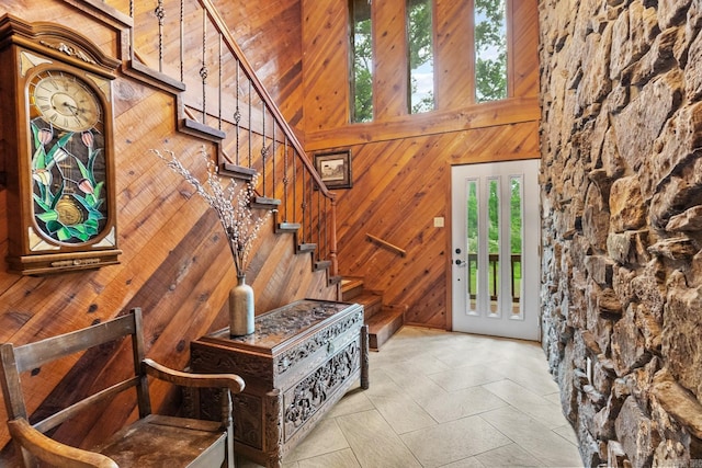 entryway with stairway, wooden walls, a high ceiling, and light tile patterned floors