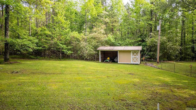 view of yard featuring a forest view, a storage shed, fence, and an outbuilding