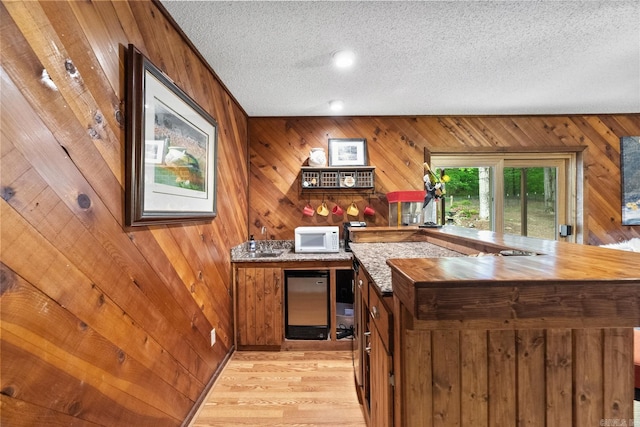 bar featuring a textured ceiling, light wood finished floors, wood walls, and white microwave