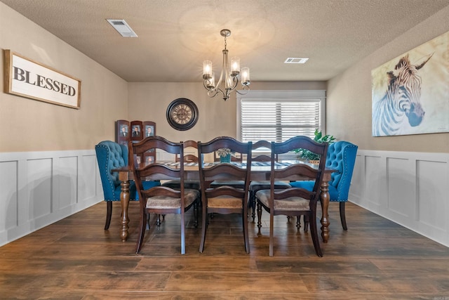 dining space featuring a textured ceiling, wood finished floors, visible vents, and an inviting chandelier