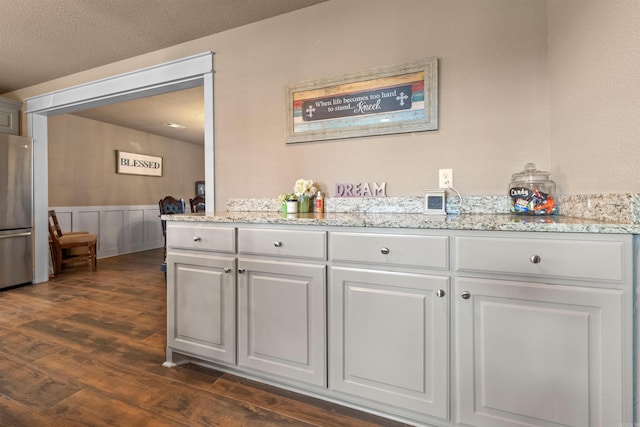 interior space with dark wood-style floors, freestanding refrigerator, wainscoting, and a decorative wall