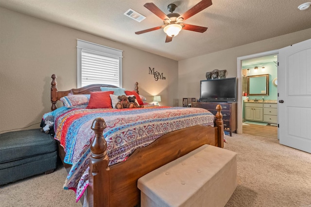 bedroom featuring visible vents, a ceiling fan, light carpet, a textured ceiling, and ensuite bath