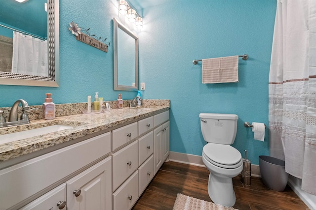 bathroom featuring double vanity, baseboards, toilet, wood finished floors, and a sink