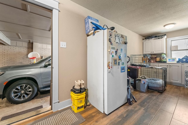 interior space with dark wood-type flooring, freestanding refrigerator, white cabinets, and a textured ceiling