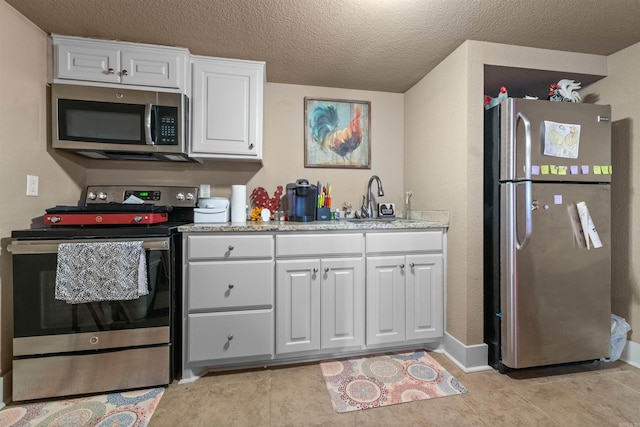 kitchen featuring light countertops, appliances with stainless steel finishes, white cabinets, a sink, and light tile patterned flooring