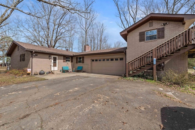 view of front of home with a garage, driveway, a chimney, stairs, and brick siding