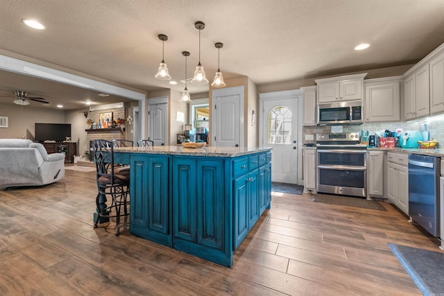 kitchen featuring blue cabinets, stainless steel appliances, dark wood-style flooring, and a center island