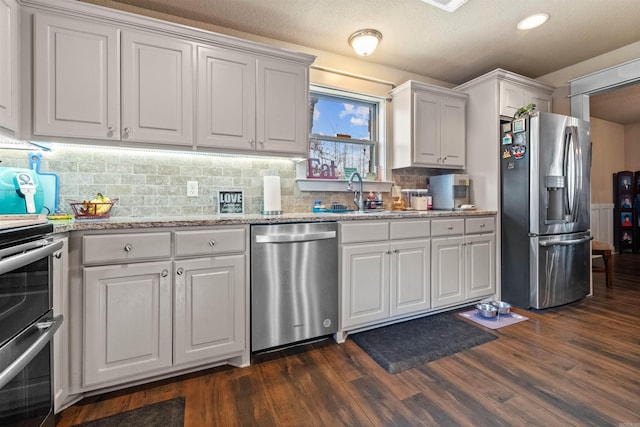 kitchen with tasteful backsplash, dark wood-style floors, appliances with stainless steel finishes, light stone counters, and white cabinetry