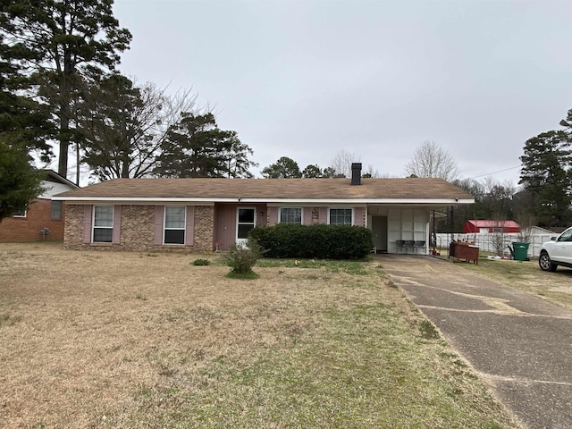 ranch-style house featuring a front yard, concrete driveway, brick siding, and a chimney