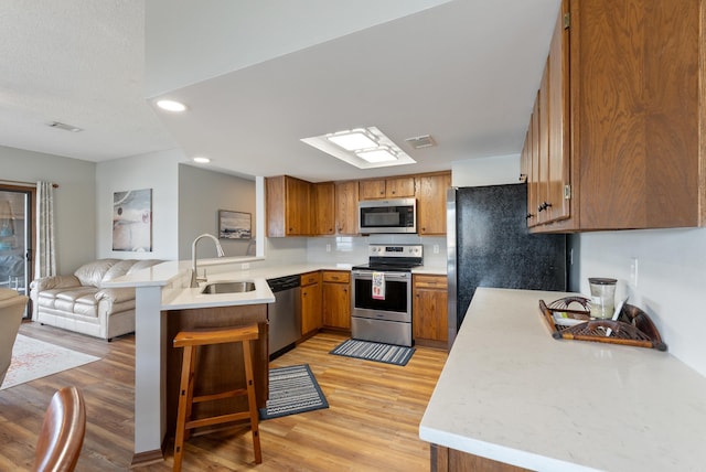 kitchen with appliances with stainless steel finishes, brown cabinetry, open floor plan, a sink, and a peninsula