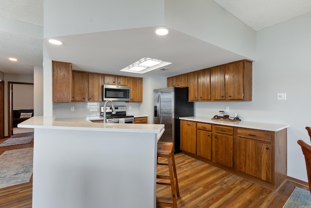 kitchen featuring a peninsula, appliances with stainless steel finishes, light wood-style floors, and brown cabinets