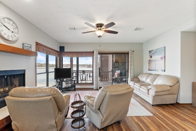 living area featuring visible vents, a ceiling fan, a tile fireplace, wood finished floors, and a textured ceiling