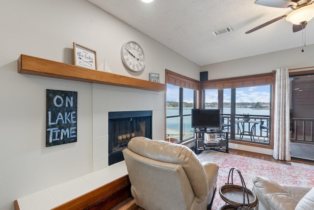 living room with a ceiling fan, a tile fireplace, visible vents, and a textured ceiling