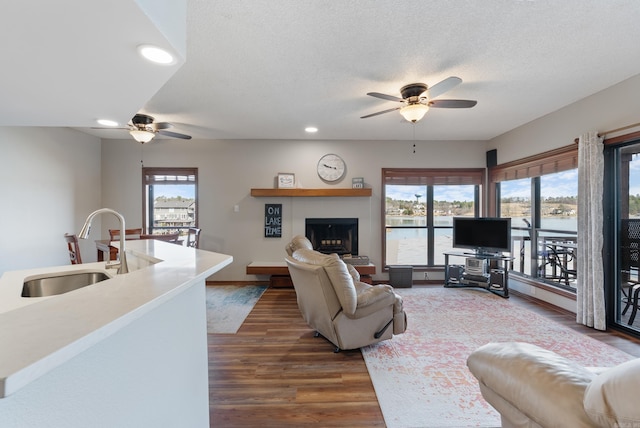 living room featuring dark wood-style floors, recessed lighting, a fireplace with raised hearth, a ceiling fan, and a textured ceiling