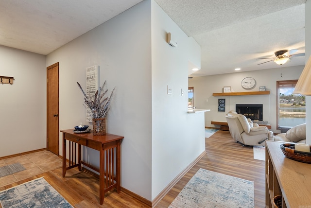 hallway featuring a textured ceiling, recessed lighting, light wood-type flooring, and baseboards