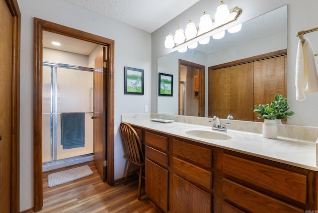 bathroom with a stall shower, a textured ceiling, wood finished floors, and vanity