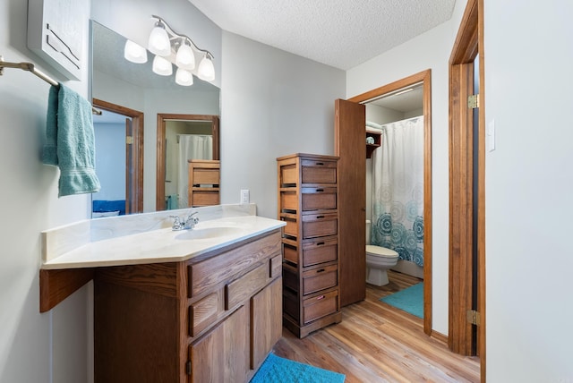 full bath featuring toilet, a shower with curtain, wood finished floors, a textured ceiling, and vanity