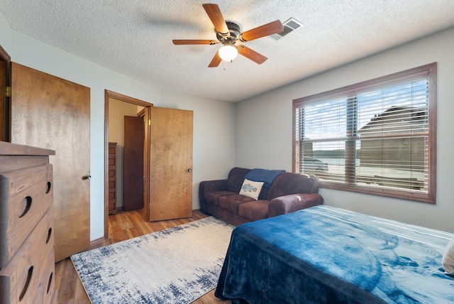 bedroom with light wood-style floors, visible vents, a textured ceiling, and a ceiling fan