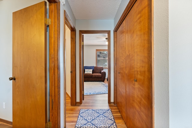 hallway with a textured ceiling, light wood-style flooring, and baseboards