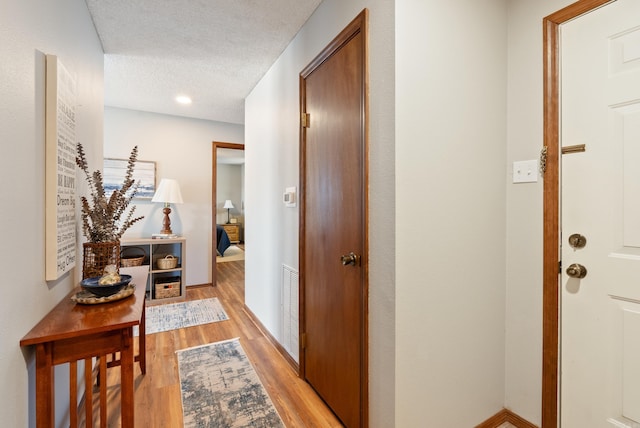 hallway featuring light wood-style floors, visible vents, a textured ceiling, and baseboards