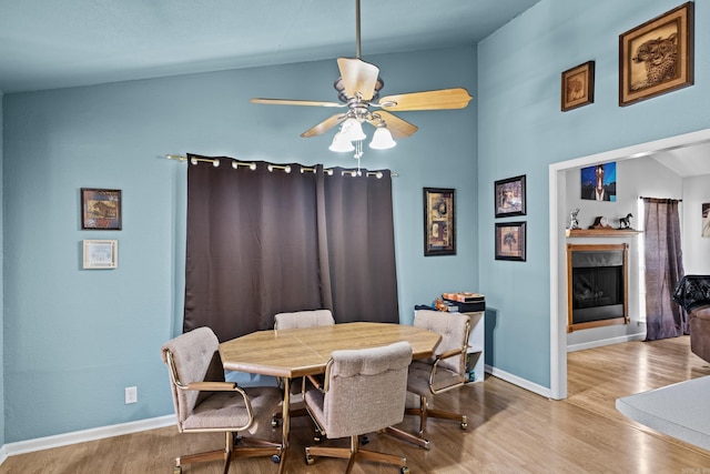 dining area featuring lofted ceiling, a fireplace, baseboards, and wood finished floors