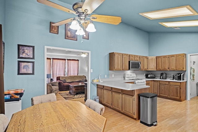 kitchen with light wood finished floors, white gas range oven, stainless steel microwave, a peninsula, and light countertops