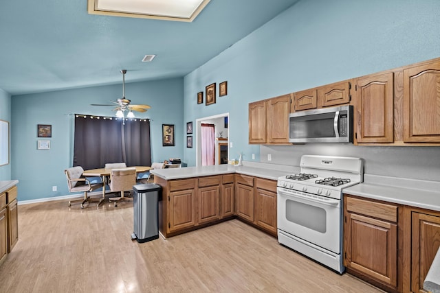 kitchen with light wood-style flooring, stainless steel microwave, vaulted ceiling, light countertops, and white gas stove