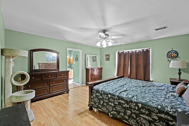 bedroom featuring light wood finished floors, baseboards, visible vents, a ceiling fan, and ensuite bath